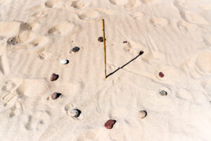 A sundial made of a stick and some rocks on a beach